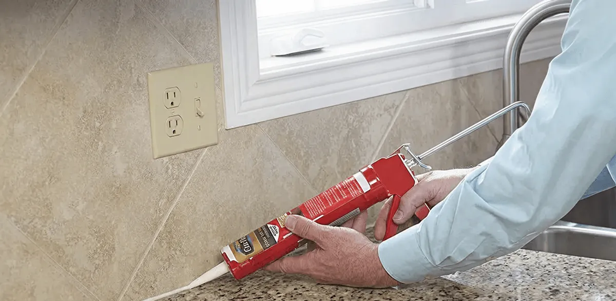Handyman applying caulk along a kitchen backsplash and countertop seam in Rochester, NY